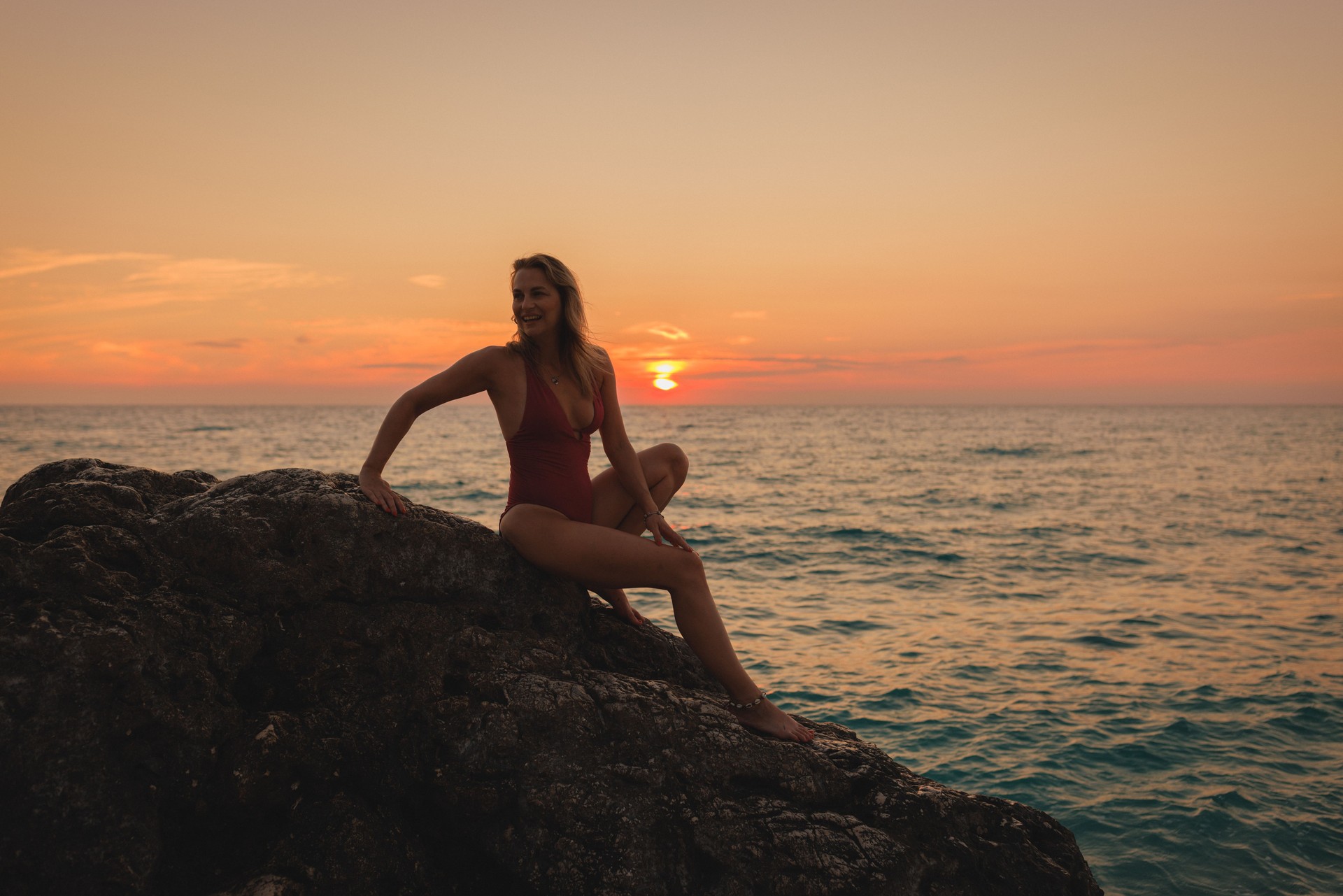 Young Woman Sitting at the Rock and Enjoying the Sunset at the Beach